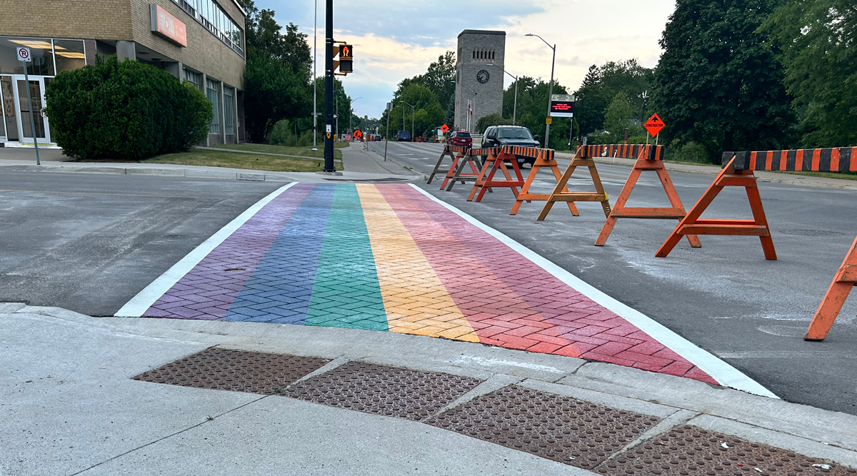 Rainbow sidewalk freshly installed with traffic barrier in front and the Carillon tower is seen in the background.