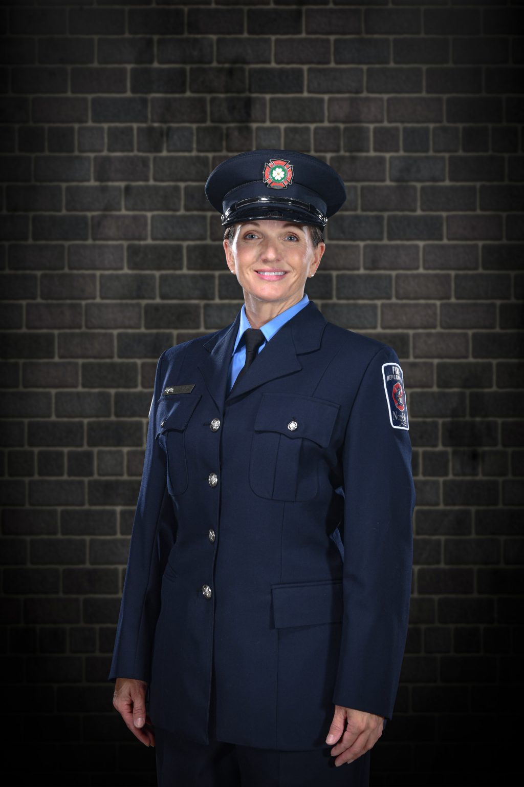 Jackie Mussel the newly promoted Norfolk County Fire captain standing against a brick wall wearing her new captain work attire.